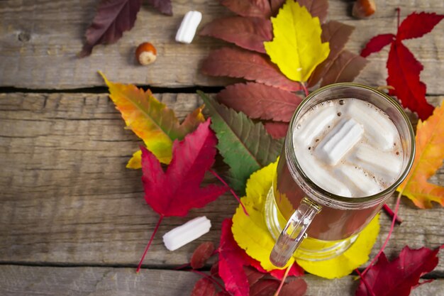 Cacao con marshmallow sul tavolo con foglie di autunno luminosi.