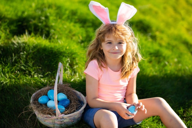 Caccia alle uova di Pasqua Coniglietto di Pasqua bambino ragazzo con viso carino Bambini a caccia di uova di Pasqua Bambino carino con cesto pasquale sull'erba