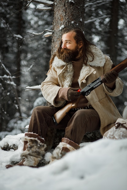 Cacciatore brutale in abiti vintage invernali con barba carica munizioni in pistola