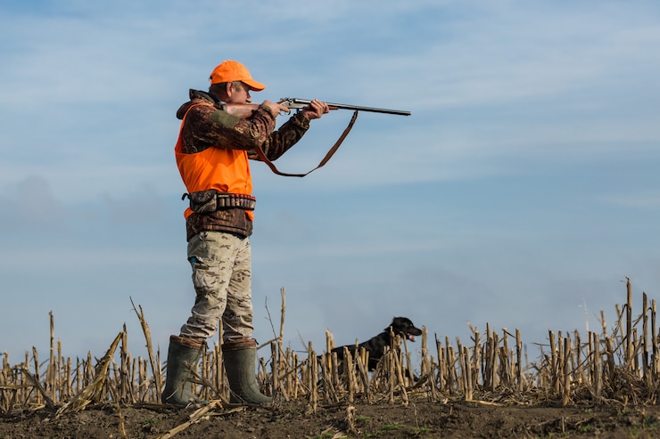 Foto cacciatore con una pistola in mano che punta in un campo
