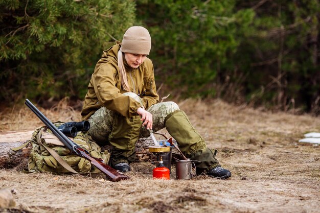 Cacciatore femminile che prepara il cibo con un bruciatore a gas portatile in una foresta d'inverno