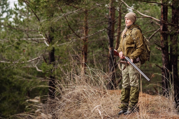 Cacciatore femminile in abiti mimetici pronto a cacciare tenendo la pistola e camminare nella foresta