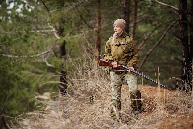 Cacciatore femminile in abiti mimetici pronto a cacciare tenendo la pistola e camminare nella foresta