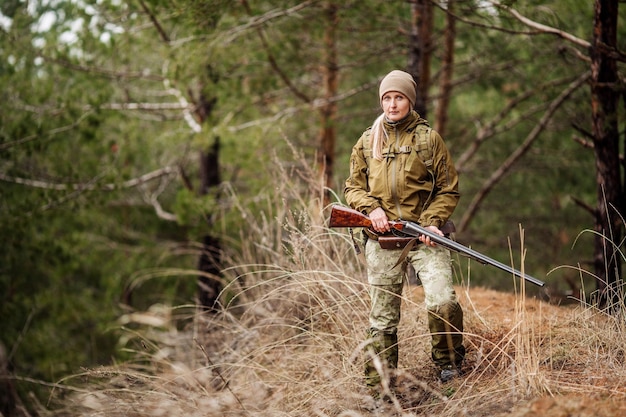 Cacciatore femminile in abiti mimetici pronto a cacciare tenendo la pistola e camminare nella foresta