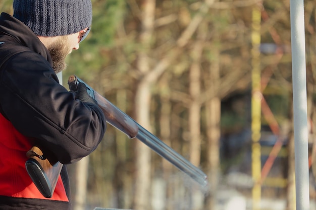 Cacciatore in mimetica con fucile nella foresta invernale. Concetto di caccia. L'uomo che fissa una riserva, in una giornata nevosa. Hunter prende la mira da una pistola nella foresta innevata