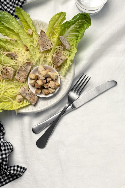Caesar Salad fatta in casa con romanina, formaggio, crostini di pane, pollo, limone e salsa. Sulla tovaglia di lino bianca