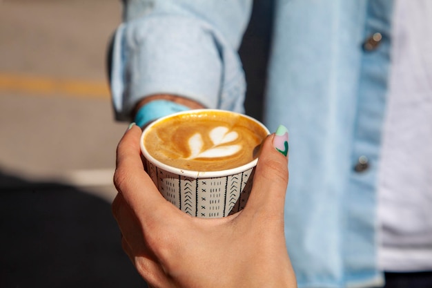 Caffè a fantasia floreale con latte. donna con unghie fantasiose che tiene il caffè in una tazza di cartone