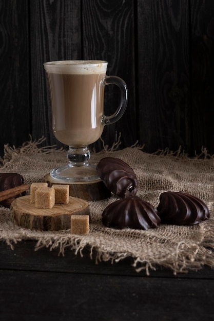 Caffè al latte con marshmallow al cioccolato e zucchero di canna su tela su fondo di legno scuro in stile rustico