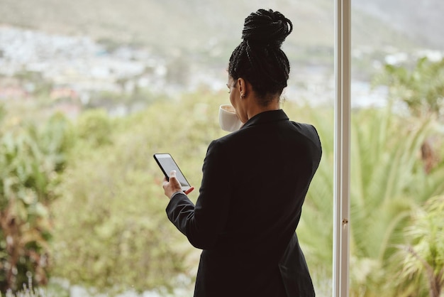 Caffè al telefono e finestra con una donna di colore d'affari che controlla i suoi social media o feed di comunicazione al mattino Rete mobile e tè con una dipendente che scrive o invia messaggi di testo vicino a una parete di vetro