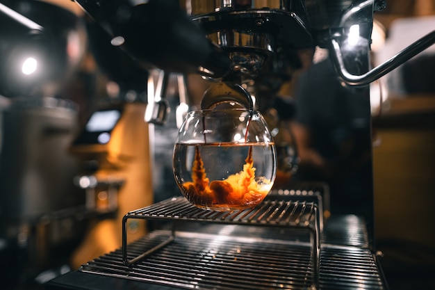 Caffè americano in una tazza dalla macchina, il caffè scende per mescolare l'acqua in un bicchiere.