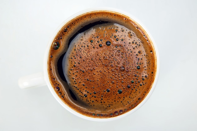 Caffè appena preparato in una tazza sul primo piano bianco del fondo