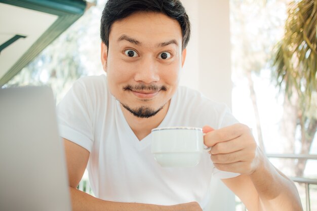 Caffè asiatico felice della bevanda dell&#39;uomo mentre lavorando con il computer.