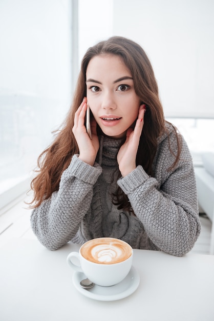 Caffè bevente confuso della giovane signora mentre parlando dal telefono