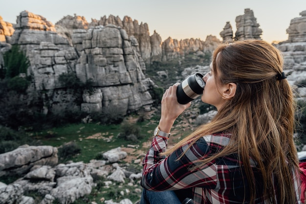 Caffè bevente dell'esploratore della giovane donna da una boccetta del thermos con le montagne nei precedenti. Concetto di avventura, escursione e gite.