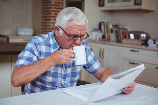 Caffè bevente dell'uomo senior mentre leggendo giornale