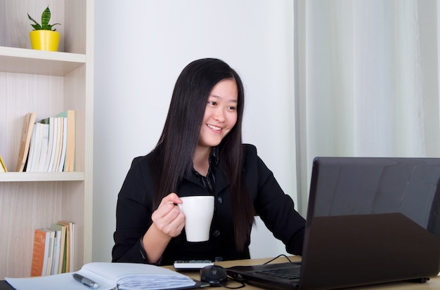 Caffè bevente della bella giovane donna di affari in ufficio