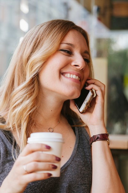 Caffè bevente della donna allegra e parlare con il suo telefono