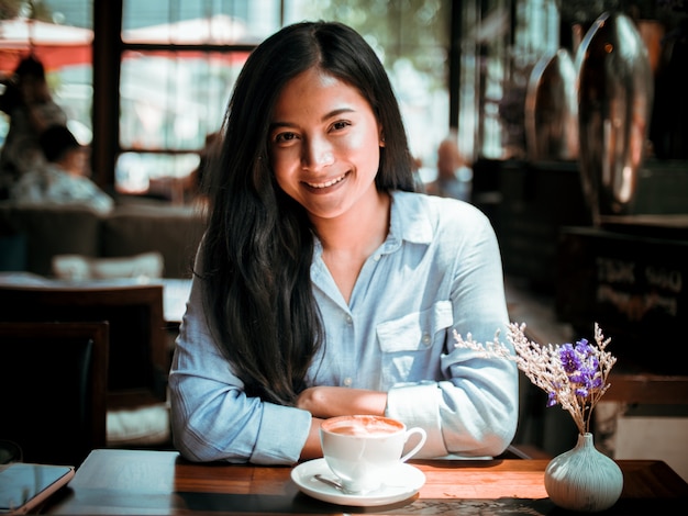 Caffè bevente della donna asiatica e lavorare con il computer portatile in caffè