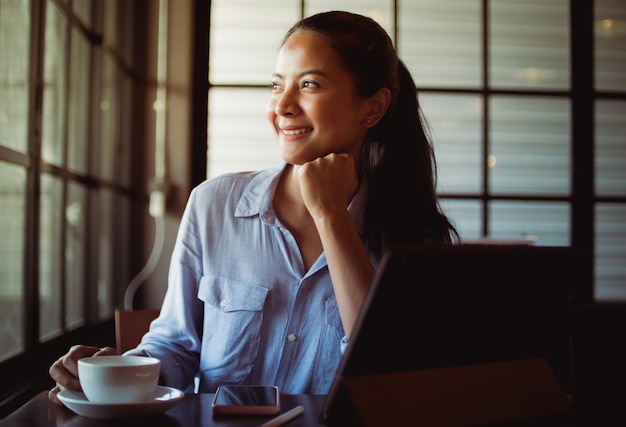 Caffè bevente della donna asiatica e lavorare con il computer portatile in caffè