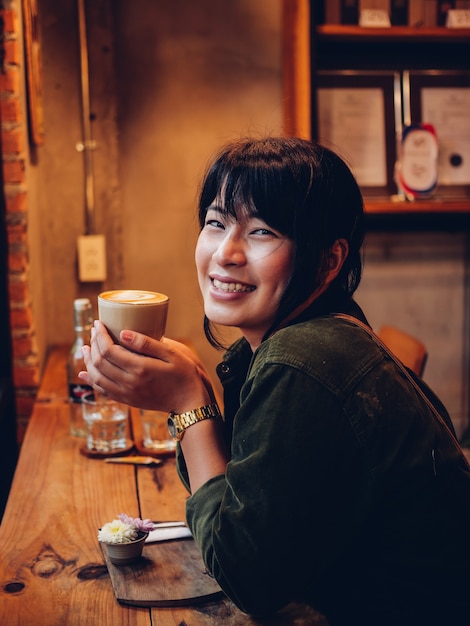 Caffè bevente della donna asiatica nel caffè della caffetteria