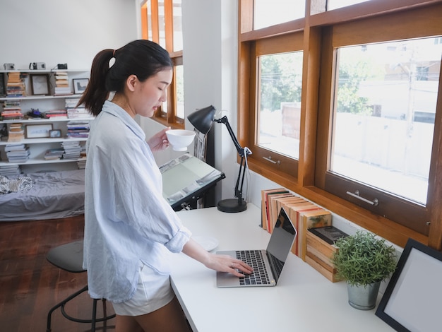 Caffè bevente della donna asiatica nella stanza di funzionamento