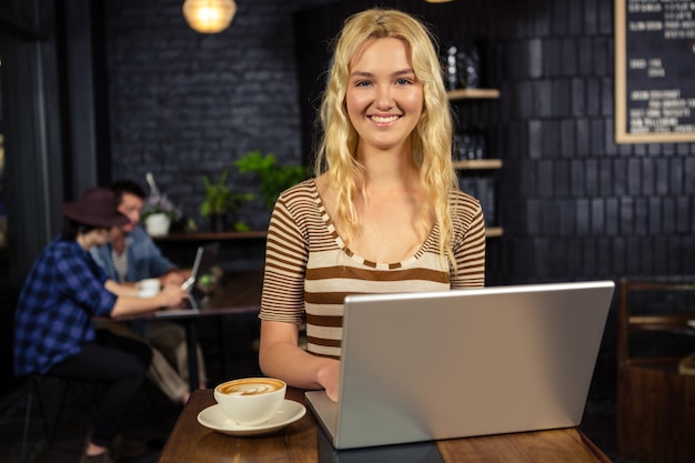 Caffè bevente della donna e computer portatile usando