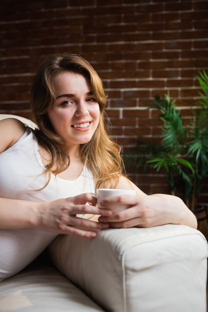 Caffè bevente della donna graziosa che si trova sullo strato nel salone