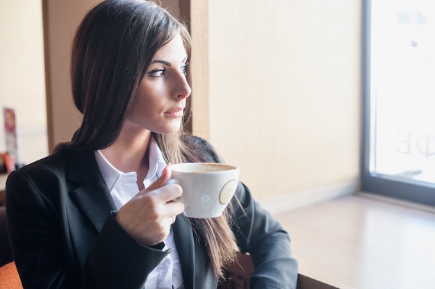 Caffè bevente della giovane donna che guarda fuori dalla finestra