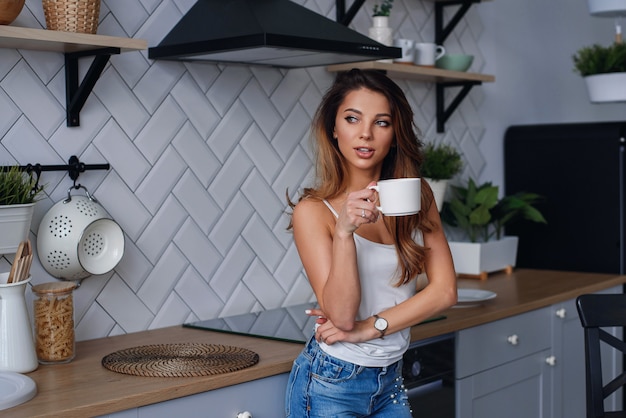 Caffè bevente della giovane donna felice sulla cucina di mattina