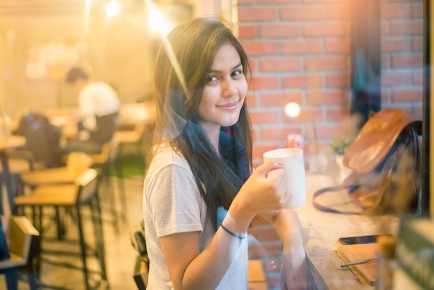 Caffè bevente dello studente universitario asiatico femminile attraente in caffetteria