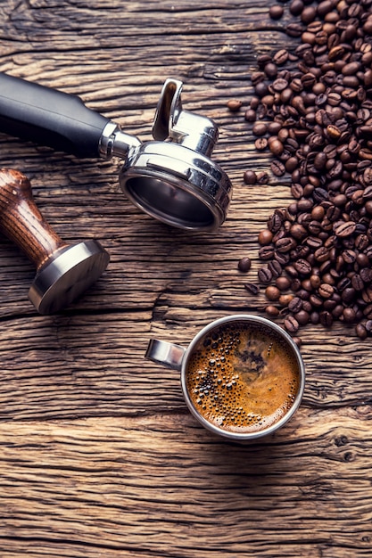 Caffè. Caffè nero con chicchi di caffè e portafiltro sul vecchio tavolo in legno di quercia.