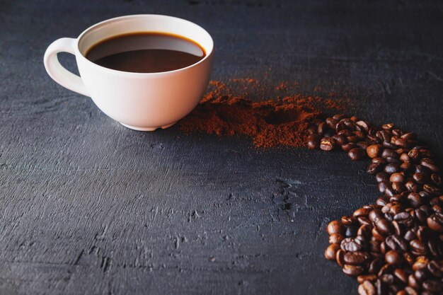 Caffè caldo con polvere di caffè e chicchi di caffè su uno sfondo nero