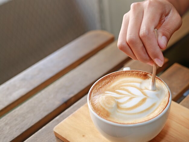 Caffè caldo del latte con il fiore di arte sulla tavola di legno.