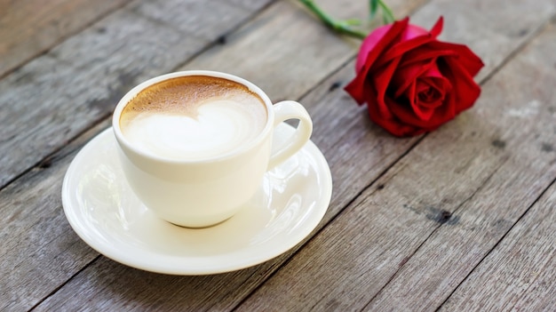 Caffè caldo e rosa rossa su un tavolo di legno.