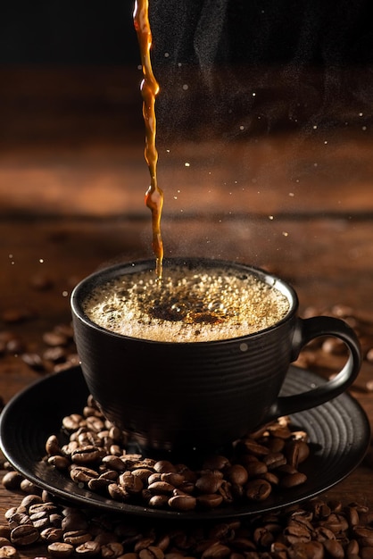 Caffè caldo e tazza nera che versa il caffè in una tazza nera sul fuoco selettivo della foto di stile alimentare scuro di legno rustico