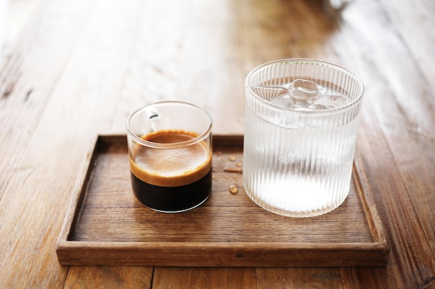 Caffè caldo e un bicchiere di ghiaccio su un vassoio di legno su un tavolo di legno