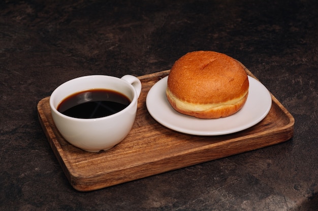 Caffè caldo in tazza bianca e ciambella fresca su un vassoio di legno