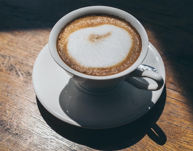 Caffè caldo in tazza di ceramica bianca rotonda sul fondo della tavola di legno