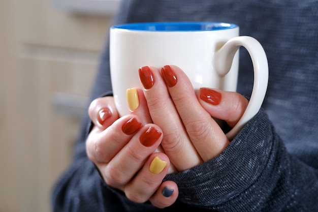 Caffè caldo in tazza. La ragazza tiene in mano una tazza di caffè. Ti scalda le mani. Seduto su una sedia a casa in quarantena.