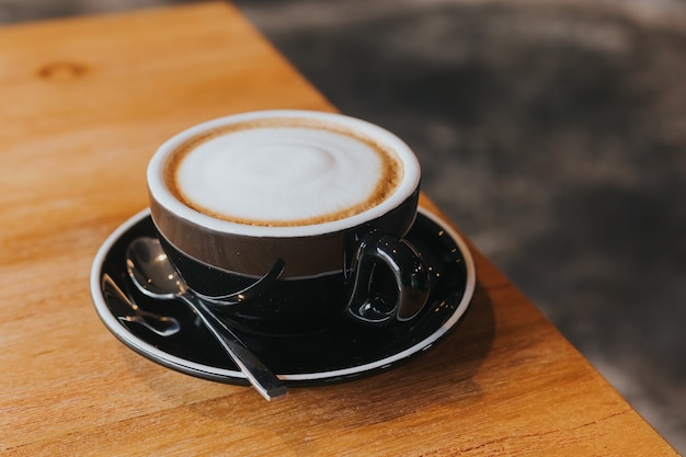 Caffè caldo in tazza nera sul tavolo di legno.