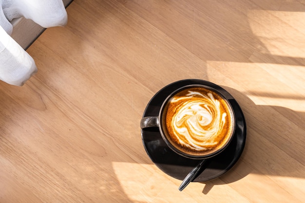 Caffè caldo latte con latte art sotto forma di schiuma di latte in tazza tazza sulla scrivania in legno sulla vista dall'alto come colazione in una caffetteria presso il concetto di lavoro aziendale cafeduring