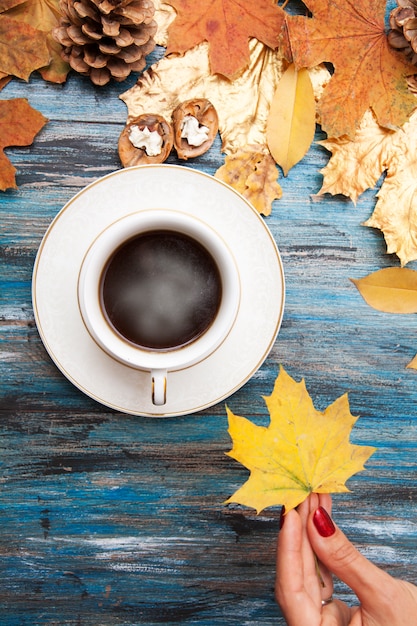 Caffè caldo su una tavola di legno, nella mano di una ragazza - foglia di acero gialla di autunno