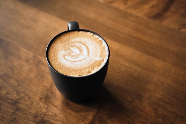 Caffè cappuccino con latte art su tavola di legno Tazza nera e bella schiuma di latte Soft focus