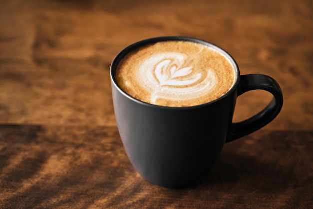 Caffè cappuccino con latte art su tavola di legno Tazza nera e bella schiuma di latte Soft focus