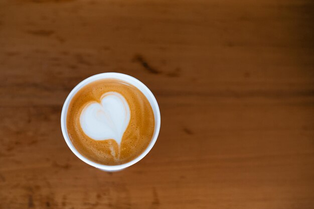 Caffè cappuccino in una tazza di carta usa e getta, vista dall'alto su uno sfondo marrone