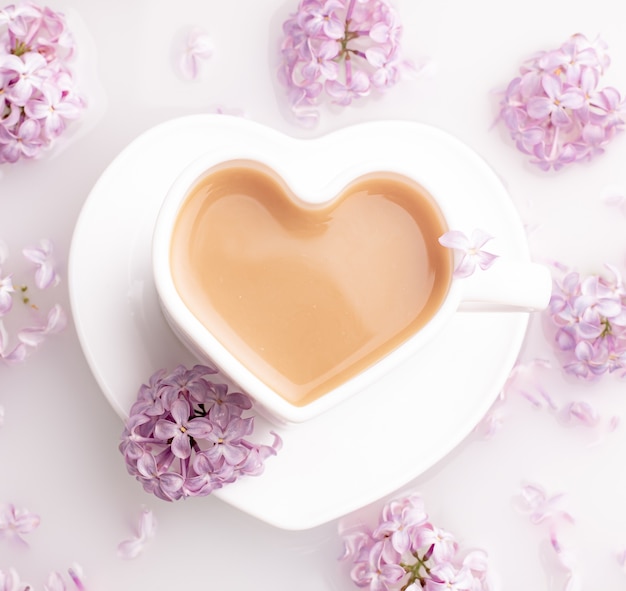 Caffè cappuccino in una tazza e un ramo di lillà su una superficie bianca. Una bevanda calda. Relax.