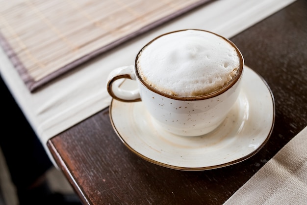 Caffè cappuccino vista laterale in tazza bianca sul fuoco tavolo in legno a schiuma bianca