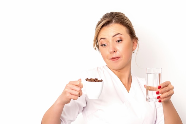 Caffè con acqua La nutrizionista femminile tiene in mano una tazza di chicchi di caffè e un bicchiere d'acqua su sfondo bianco