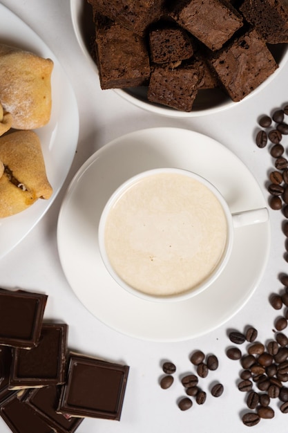 Caffe' con cappuccino al latte in una tazza bianca, cioccolato e torta su uno sfondo bianco