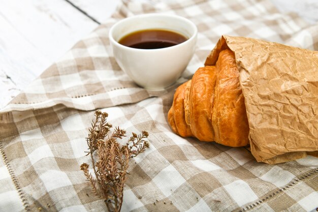 Caffè con cornetto. l'inizio della mattina. Una tazza di caffè. cornetto francese fresco. Tazza di caffè e croissant al forno freschi su un fondo di legno. Vista dall'alto